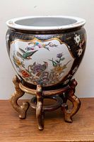Front view of the large Chinese fishbowl planter pot on its wooden stand, showing painted birds, flowers, and fish