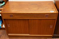 Front view of teak veneer cabinet showing sliding doors and recessed handles.