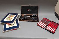 Wide view featuring all items including the Wüsthof cutting tool set in wooden box, two sets of vintage forks and knives in original boxes, and Pimpernel cork placemats stacked.
