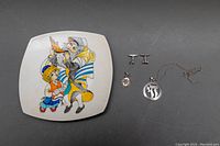 Photo of signed hand-painted ceramic plate with colorful Jewish-themed illustration alongside sterling silver jewelry including Chai pendant necklace, cufflinks, and Star of David pendant.