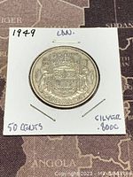 Reverse side of the coin showing the Canadian coat of arms with 'CANADA 1949 50 CENTS' inscribed, coin in stapled cardboard holder with handwritten notes.