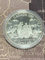 Obverse side of the coin showing explorers on the Mackenzie River in a canoe with detailed scenery and inscriptions.