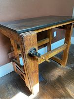 Side angle photo of the antique wooden workbench showing the wood's aged surface, metal handle, and granite slab top.