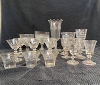 Front view of the assorted EAPG glassware showing all glasses and the vase on black cloth background.