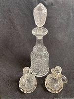 Front view of tall glass decanter with stopper and two smaller oil and vinegar bottles on either side on black textured background