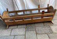 Photo showing side and end view of the wooden cradle, highlighting natural wood finish and slat railings.