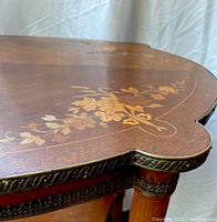 Close-up image showing detailed floral wood inlay and metal trim decoration on the table edge.