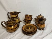 Golden brown lusterware tea set including teapot, sugar bowl, cups, pitchers, and plates.
