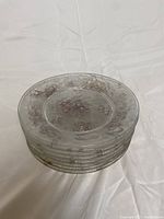 Stack of 8 transparent glass plates with visible floral pattern and no chips.