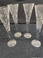 Four Waterford crystal champagne flutes standing on black fabric, showing their general shape and intricate etching.