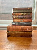 Stack of nine antique books showing condition and varied sizes.