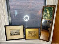 Full view of the lot showing two framed prints standing next to a tall rectangular mirror with print of woman and dog on top.