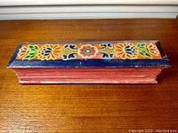 Top view of the closed carved wooden book cover with colorful floral designs on a wooden surface.