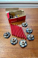 Seven small blue porcelain Wade candlestick holders arranged with seven red twisted wax candles on wooden surface, vintage cardboard box visible in background