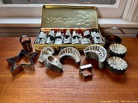 Overview of vintage metal candy and cookie molds arranged on wooden surface with vintage Fry's chocolate tin behind containing zodiac sign molds