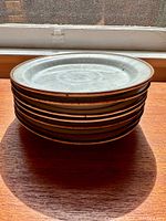 Stack of seven Dansk salad plates showing the rustic glaze and brown rim under natural light.