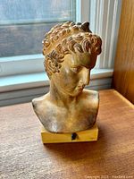 Front and angled views of bronze colored bust sculpture of the Ephebe of Marathon on wooden base by a window, showing detailed features, hair curls, and the bust form.