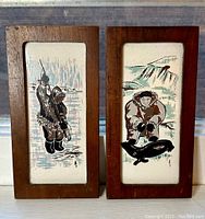 Two Eskimo art ceramic tiles mounted in walnut frames showing fishing scenes and Eskimo figures with seals. Photos show detailed artwork and condition of frames.