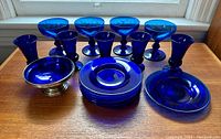 Overview of entire lot on wood surface including champagne glasses, stemmed bowls, cobalt blue plates and a bowl with silver base