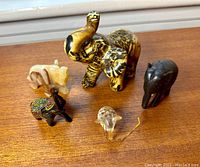 All six miniature elephant figurines arranged on wooden surface, showing varied colors and materials.