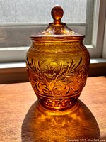 Front view of amber glass sandwich pattern biscuit cookie jar with ball handle lid on wooden surface with sunlight backlight.