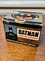 Box with Batman logo, image of Batman in costume, and text indicating 143 glossy cards and 22 stickers. Box is worn with creases and scuff marks.