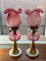 Pair of cranberry hobnail glass lamps on windowsill, full front view