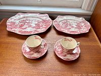 Image of two tea cups with matching saucers and two serving trays on wooden surface near a window.