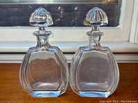Front view of the pair of clear crystal decanters with differently shaped stoppers on a windowsill showing no visible damage.