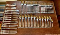 Full set of silver-plated flatware laid out on a wooden surface showing knives, forks, spoons, and small knives.