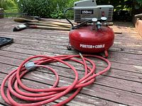 Side view of red Porter Cable air compressor tank connected to gray motor with red hose coiled beside it on wooden deck.