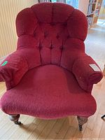 Front view of red upholstered tufted armchair with wooden legs and casters on front