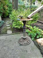 Full view of the iron bird bath placed on a concrete surface with surrounding greenery.