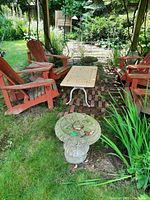 Full view of one cement table base in an outdoor garden setting beside red Adirondack chairs and a small table.