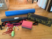Yoga mats, foam roller, skipping ropes, resistance straps, and yoga block arranged on wooden floor.