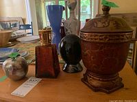 Lot featuring amber glass lamp with gold wick holder, metal apple-shaped bowl with spoon, and dark polished stone on stand.