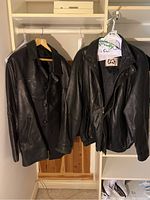 Two men's black leather jackets hanging on a rack, one bomber style and one dress style.