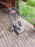 Full view of gas-powered power washer with Honda GC160 engine, hose coiled and attached on frame, mounted on a two-wheeled metal frame.