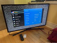 Samsung LED TV showing the settings screen with Picture menu and a remote on the floor in front of it.