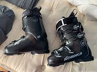 Pair of black Nordica Speedmachine 130 Carbon ski boots shown from side angle with buckles and branding visible.