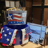 Metal bins with Americana designs next to framed artwork and an American flag draped over the blue bin.