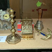 Photo showing the collection of brass candlestick, wooden handle bell, brass anchor door knocker, resin wolf clock, and wooden match dispenser.