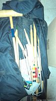 Black carrying bag open showing multiple wooden croquet mallets with colored tape on handles, croquet balls, and metal wickets inside.