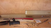 Long Gerber carving tool in original box with sharpener and various small clamps and scissors on a wood background