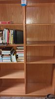 Close-up photo of one side of the light oak double bookcase showing shelves partially filled with books, shelf spaces, and wood grain.