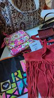Photo showing red suede fringe bag, pink Vera Bradley bag with floral print, black quilted tote, brown carpet bag, and other small bags and wallets on a table.