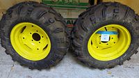 Two John Deere tractor tires side by side, showing full tread and yellow 5-lug rims
