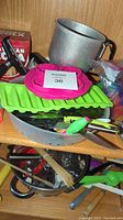 Photo of assorted kitchen items on shelf including metal measuring cup, green ice cube trays, skewers, spatulas, and various utensils.