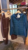 Both coats hanging on wooden hangers on a wooden rod in a room with visible shelving and storage items.