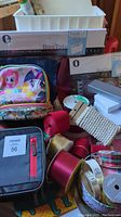 Photo showing assorted lunch bags including My Little Pony and black with red accents, various decorative ribbon spools, BoxTote storage totes, and small white jewelry boxes.